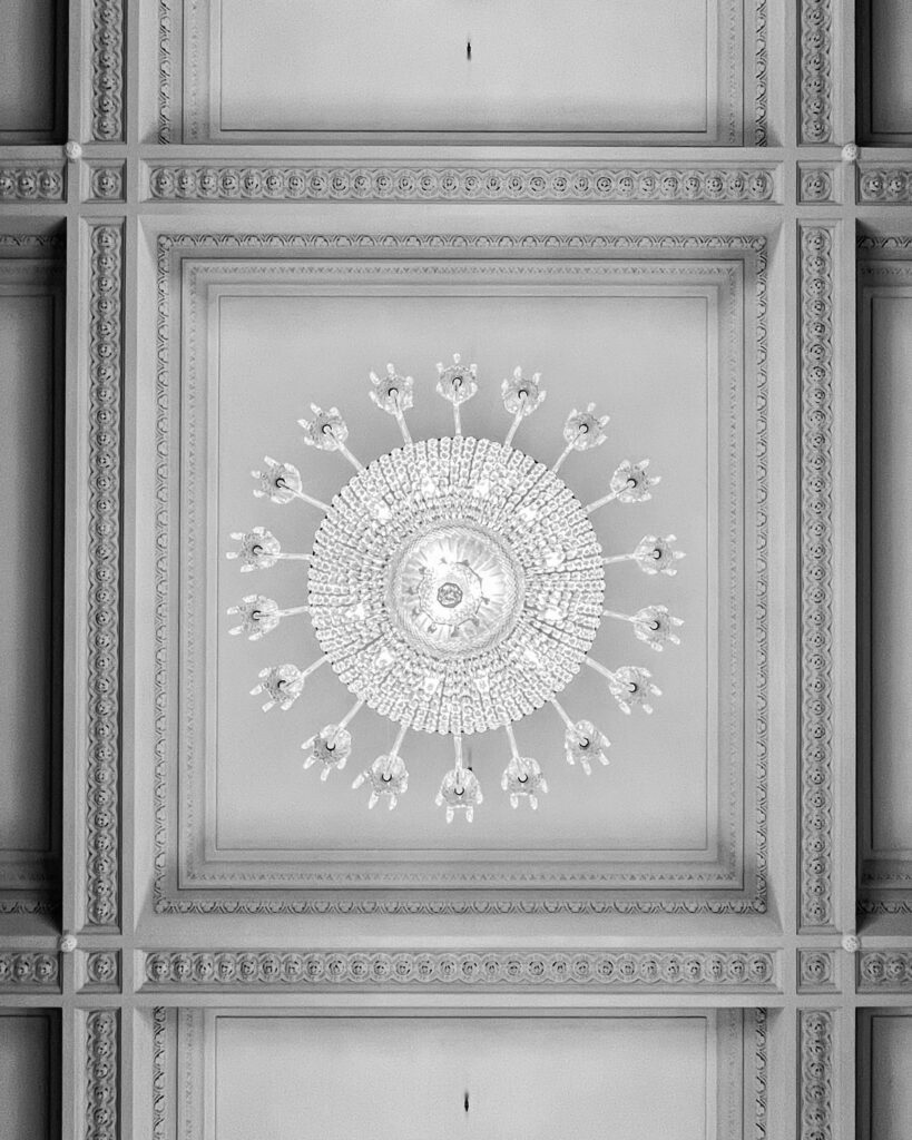 Black and white photo of a decorative chandelier on an intricately patterned ceiling in Dublin.